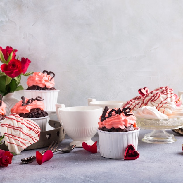 Hermoso cupcake de chocolate, crema rosa, galletas de merengue y rosas rojas sobre la superficie de piedra gris. San Valentín, día de la madre, concepto de boda con espacio de copia