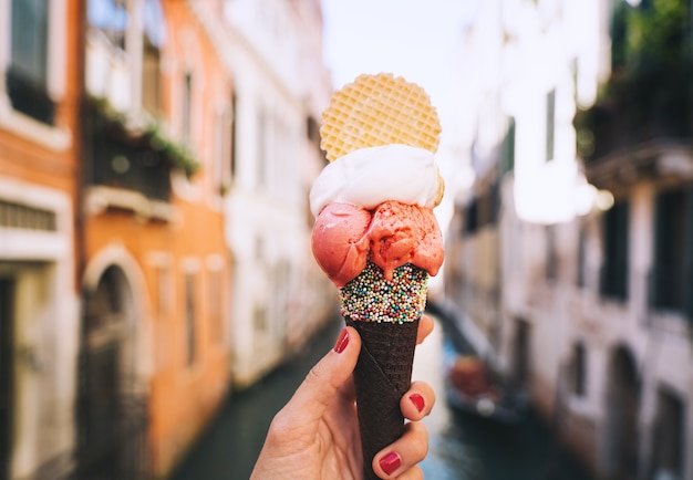 Hermoso y delicioso helado italiano en cono de waffle frente a calles y puentes de Venecia