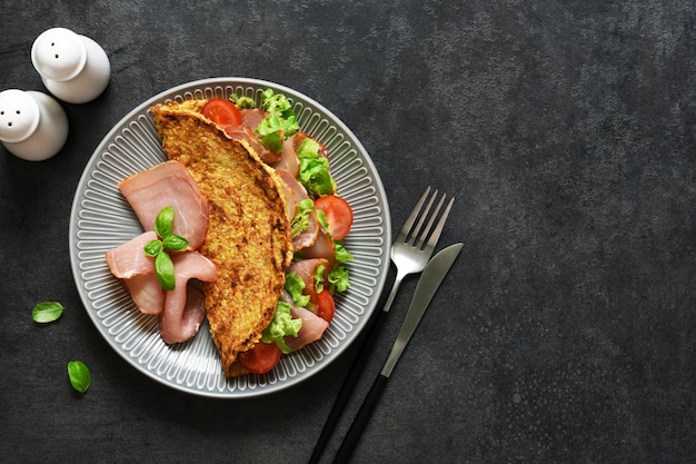 Hermoso desayuno con tomate, jamón y ensalada sobre un fondo negro. Panqueque con relleno, vista superior.