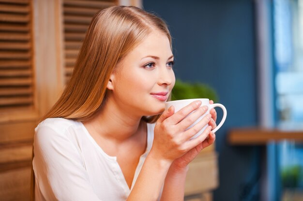 Hermoso día soñador. Vista lateral del pensativo joven disfrutando de un café en la cafetería