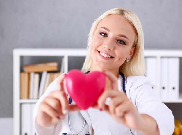 Hermoso doctor sonriente espera en brazos corazón rojo