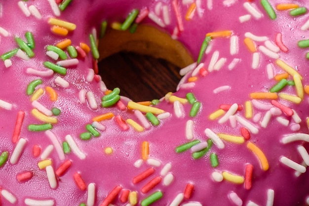 Un hermoso donut con glaseado rosa y espolvoreado de colores sobre un fondo de hormigón oscuro