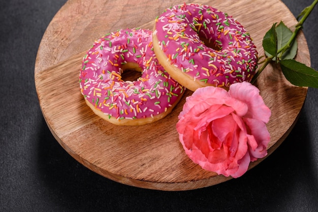 Un hermoso donut con glaseado rosa y espolvoreado de colores sobre un fondo de hormigón oscuro