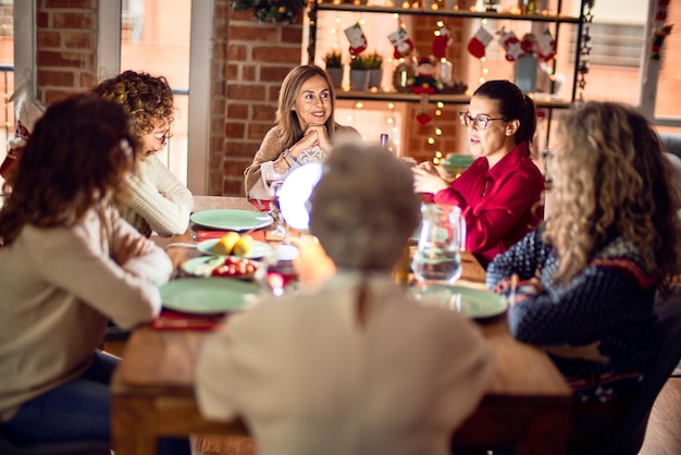Hermoso grupo de mujeres sonriendo felices y confiadas comiendo pavo asado celebrando la navidad en casa