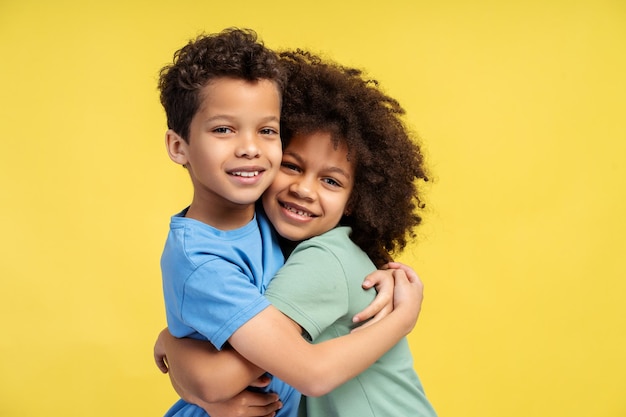 Hermoso hermano y hermana abrazados mirando a la cámara posando en el estudio aislados sobre un fondo amarillo