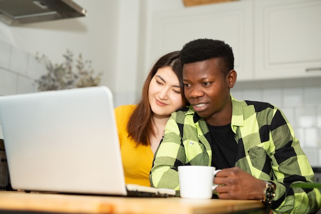 Hermoso hombre africano y mujer asiática en la cocina con laptop