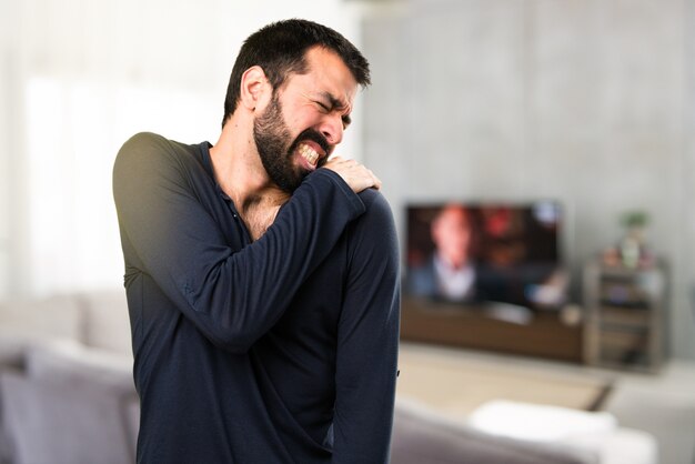 Hermoso hombre con barba con dolor de hombro dentro de la casa