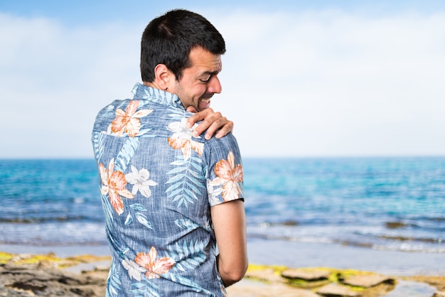 Foto hermoso hombre con camisa de flor con dolor de hombro en la playa