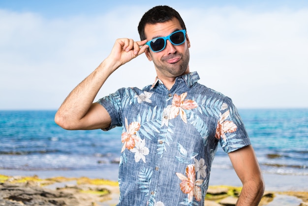 Hermoso hombre con camisa de flor con gafas de sol en la playa