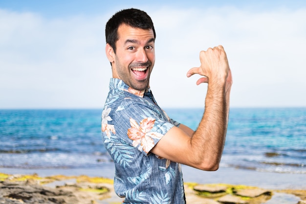 Hermoso hombre con camisa de flor orgulloso de sí mismo en la playa