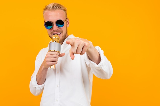 Hermoso hombre caucásico con gafas canta canciones en karaoke con micrófono aislado en amarillo