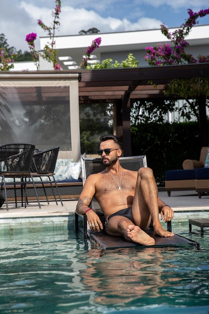 hermoso hombre dentro de la piscina sentado en una silla, hombre con una gran barba, bañadores y tatuajes