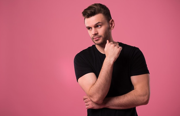 Hermoso hombre elegante, confiado y serio en camiseta negra está posando sobre fondo rosa