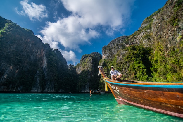 Hermoso hombre navegando en un barco de madera retro por el mar de Andamán y detrás de él se puede ver la isla de Ko Phi Phi Lee.