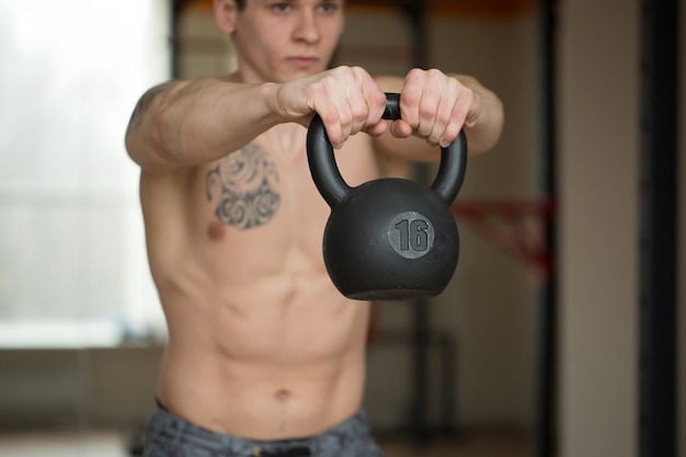 Hermoso hombre se pone en cuclillas con pesas rusas en el gimnasio