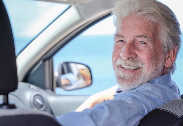 Hermoso hombre senior de pelo blanco sentado dentro del coche mirando a la cámara