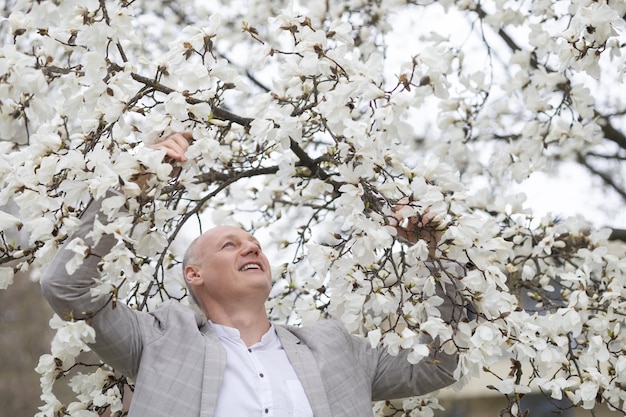 Hermoso hombre sonriente en el fondo de la magnolia floreciente blanca