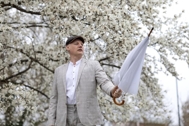 Hermoso hombre sonriente con paraguas en medio de magnolia de flores blancas