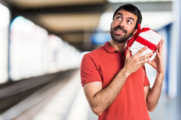 Hermoso hombre sosteniendo un regalo sobre fondo desenfocado