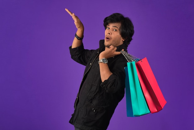 Hermoso joven apuesto indio sosteniendo y posando con bolsas de compras en un fondo morado