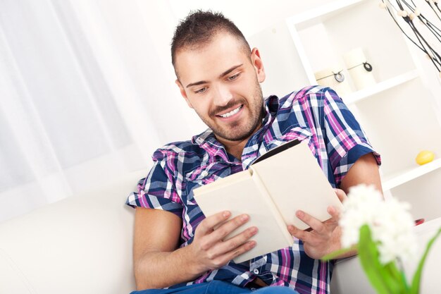 Hermoso joven descansando con un libro en casa.