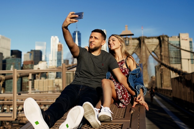 Hermoso joven y una mujer posan en el puente de Brooklyn en los rayos del sol de la mañana