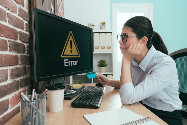 Foto hermoso joven oficinista con tarjeta de crédito y mirando la computadora pensando en la solución del problema de error del sistema de comercio electrónico.