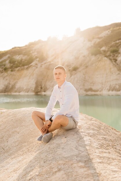 Hermoso joven viaja por el mundo cerca de un lago azul y arena al atardecer