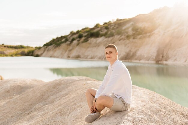 Hermoso joven viaja por el mundo cerca de un lago azul y arena al atardecer