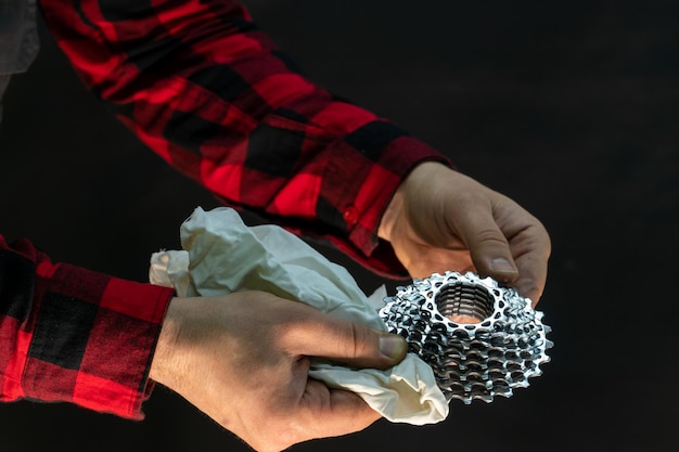 Un hermoso mecánico de bicicletas de moda con una camisa a cuadros roja sostiene piezas de bicicleta en sus manos Casete de bicicleta y las manos del mecánico se cierran sobre un fondo negro en un estudio fotográfico Reparación de bicicletas