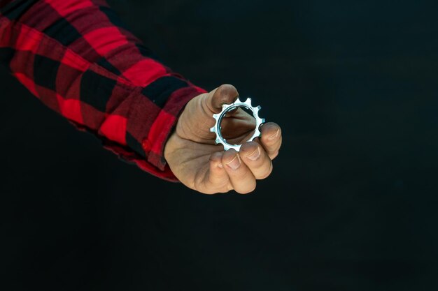 Foto un hermoso mecánico de bicicletas de moda con una camisa a cuadros roja sostiene piezas de bicicleta en sus manos casete de bicicleta y las manos del mecánico se cierran sobre un fondo negro en un estudio fotográfico reparación de bicicletas