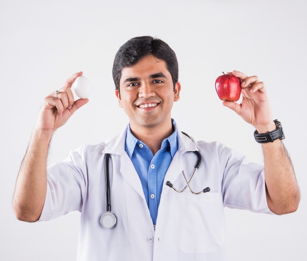 Hermoso médico indio mostrando o comiendo manzana roja fresca. que se encuentran aisladas sobre fondo azul