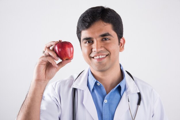 Hermoso médico indio mostrando o comiendo manzana roja fresca. que se encuentran aisladas sobre fondo azul