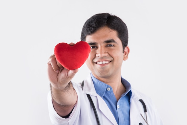 Hermoso médico indio sosteniendo un corazón de peluche rojo como un concepto de cuidado del corazón. que se encuentran aisladas sobre fondo azul