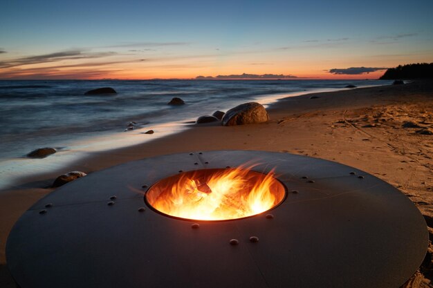 El hermoso metal alrededor de una chimenea se encuentra en la costa arenosa con un maremoto al atardecer piedras s...