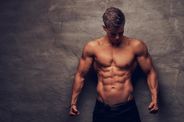 Hermoso modelo de hombre joven sin camisa con buen cuerpo musculoso posando en un estudio. Aislado en un fondo oscuro.