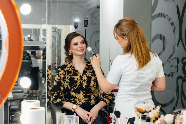 En un hermoso y moderno salón de belleza, un estilista de maquillaje profesional hace maquillaje para una niña.