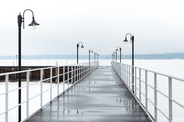 Hermoso muelle vacío en invierno en el ríoLa nieve se derrite comienza la primavera