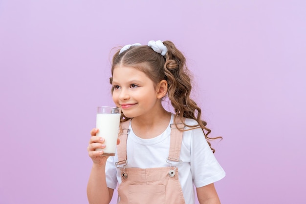 Hermoso niño bebe leche para el desayuno. Una niña con el pelo rizado sostiene un vaso de leche de vaca.