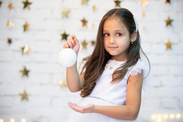 Un hermoso niño con una bola de Navidad Chica con un vestido blanco con un juguete de Navidad