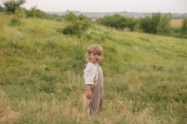 Un hermoso niño con cabello rubio y cabello rizado descansa en la naturaleza junto al río.