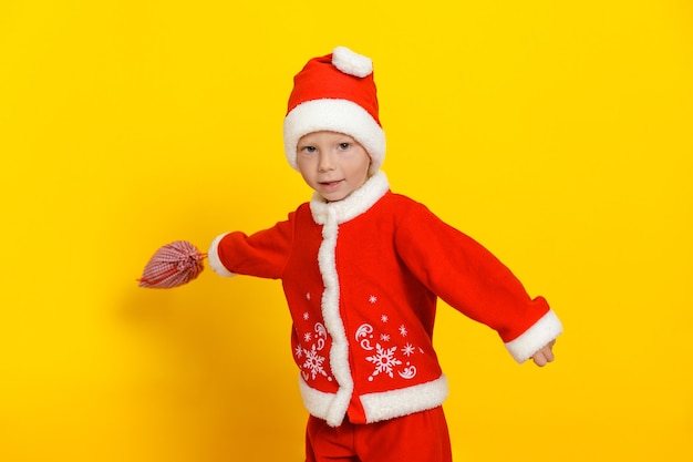 Hermoso niño caucásico agitando un saco de regalos sobre un fondo amarillo vestido como Santa Claus.