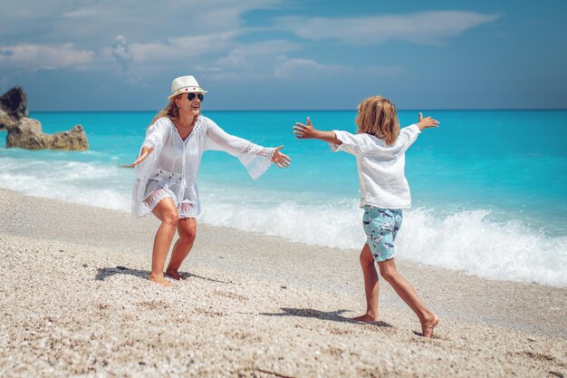 Hermoso niño disfrutando con su madre en la playa. Corre por la playa a los brazos de su madre.