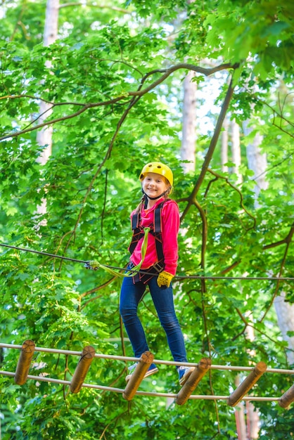 Hermoso niño escalando y divirtiéndose en el parque de aventuras Senderismo en el parque de cuerdas niña en equipo de seguridad Niño trepando árboles en el parque Niño lindo niño