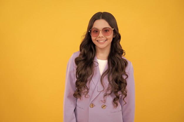 Hermoso niño feliz con elegante chaqueta morada y gafas de sol con estilo de fondo amarillo