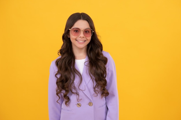 Hermoso niño feliz con el pelo rizado en una elegante chaqueta morada y gafas de sol con un estilo de fondo amarillo