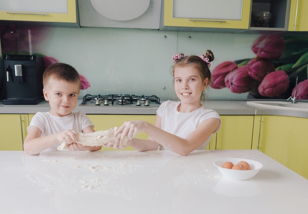 Hermoso niño y niña estirando la masa en la cocina jugando y divirtiéndose mientras cocina. niños felices felices