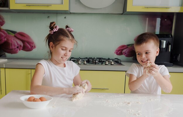 Hermoso niño y niña estirando la masa en la cocina jugando y divirtiéndose mientras cocina. niños felices felices