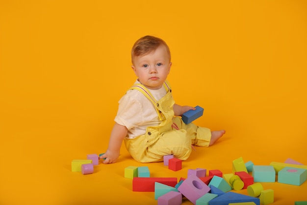 un hermoso niño de ojos azules con un traje amarillo juega con juguetes de colores