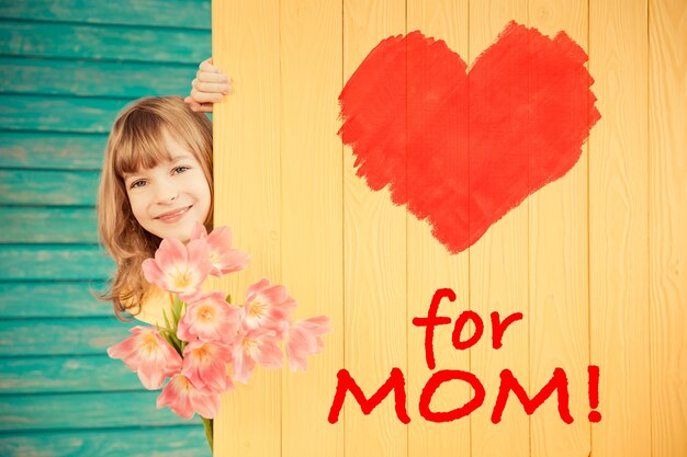 Hermoso niño con ramo de flores escondido detrás de fondo de madera concepto del día de la madre